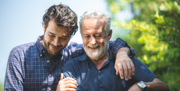 Two men holding each other while walking outside. One is middle aged and one is older.