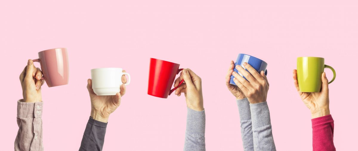 Many different hands holding multi colored cups of coffee on a pink background.