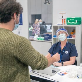 Man at a vaccination clinic talking to a nurse wearing a mask