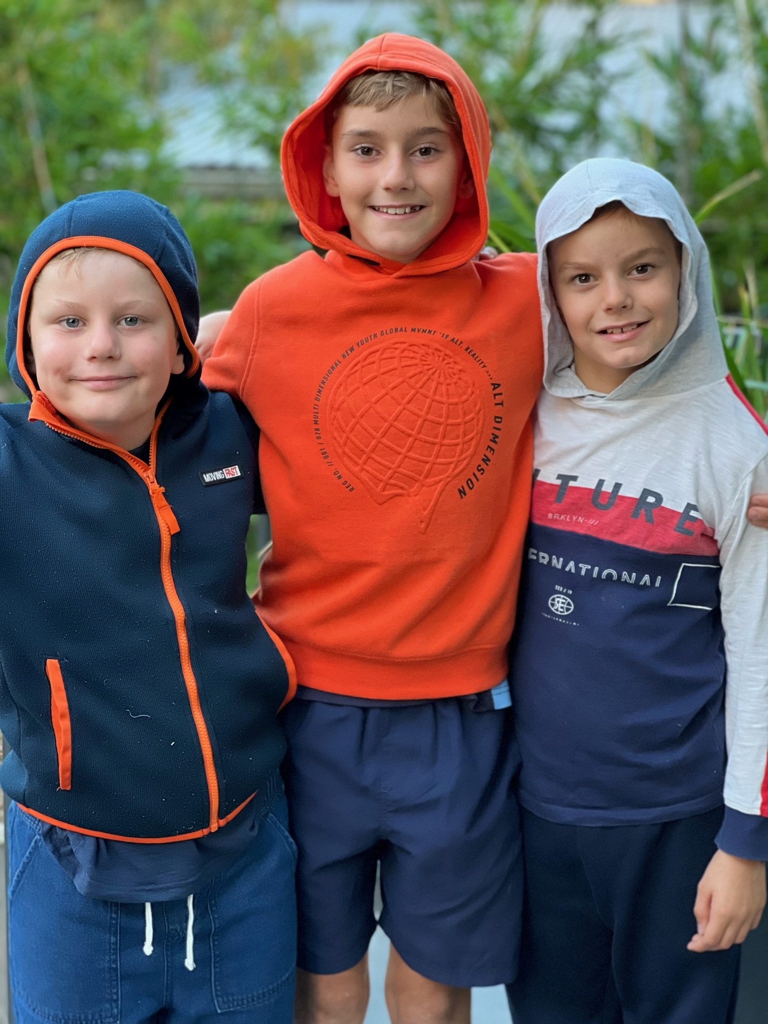 Fletcher, Felix and Sebastian are wearing hoodies outside. Felix has his arms around his brothers.