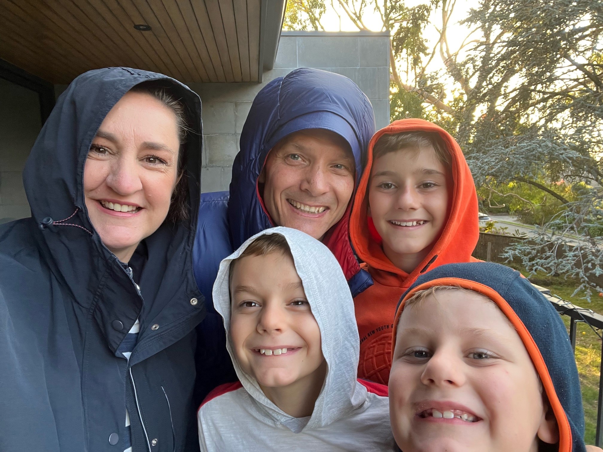 Felix and his family, smiling and wearing hoodies outside their home