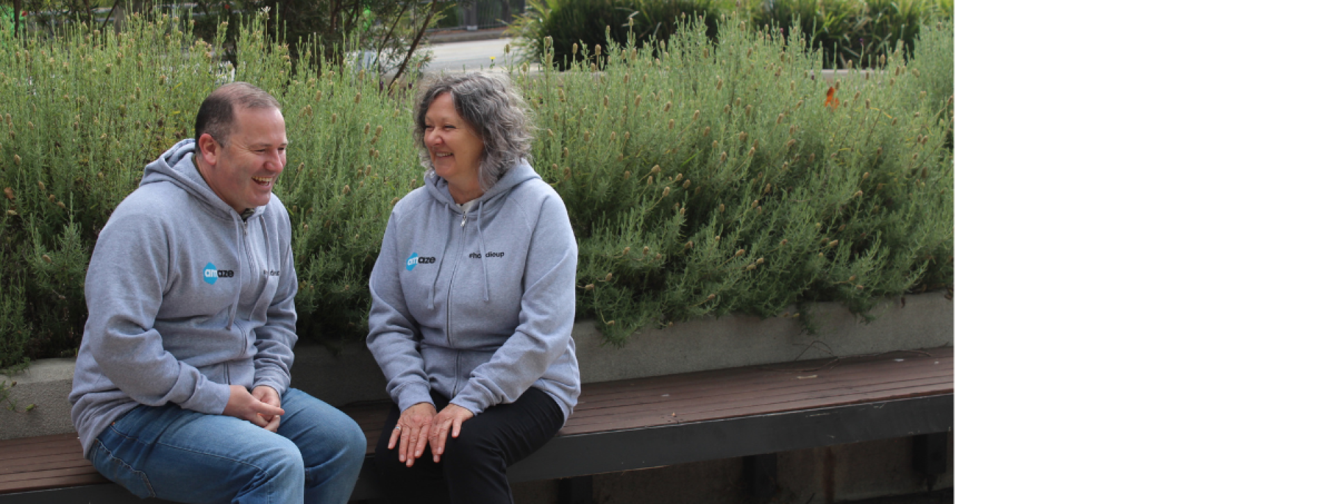 David and Jenny sitting outside wearing hoodies and smiling at one another