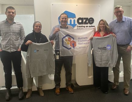 A group of Amaze employees standing with a group of Autism Community Network Australia employees in front of the Amaze business sign. 