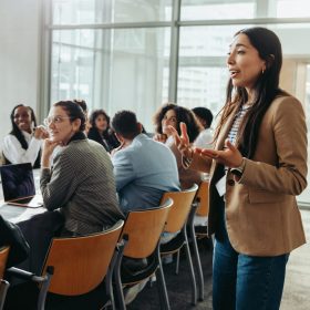 Workers in an office at a desk with one person standing and addressing someone off camera