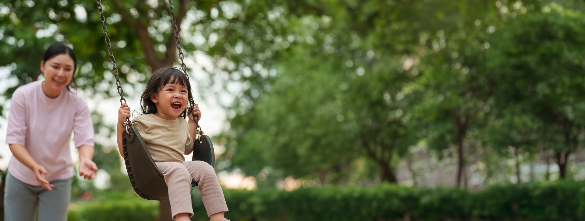 A happy child being pushed on a swing by their mother.